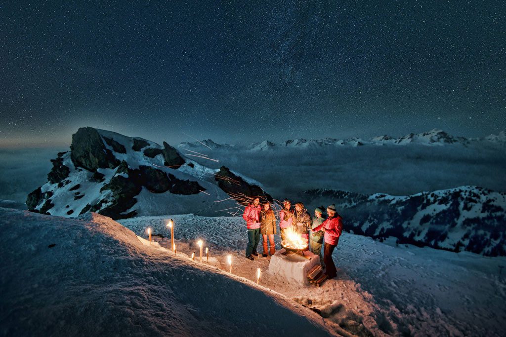 Gruppe auf Gipfel bei Nacht mit Fackeln und Feuerstelle