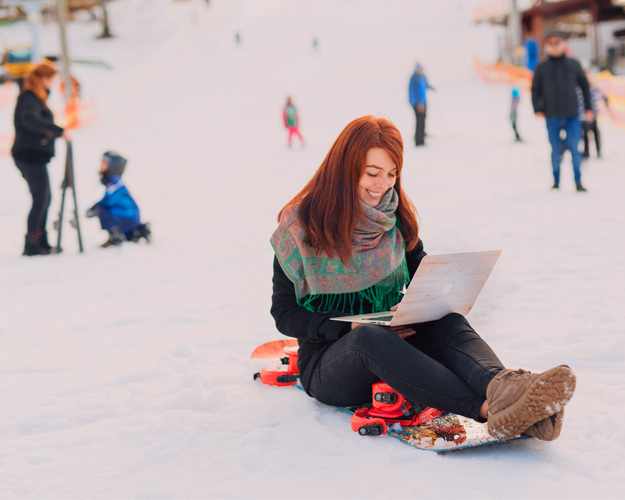 Snowboarderin sitzt auf Board und schreibt in Laptop